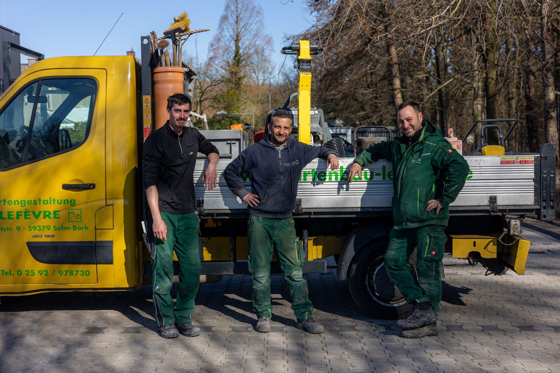 Drei Männer posieren für ein Foto vor einem gelben Lastwagen