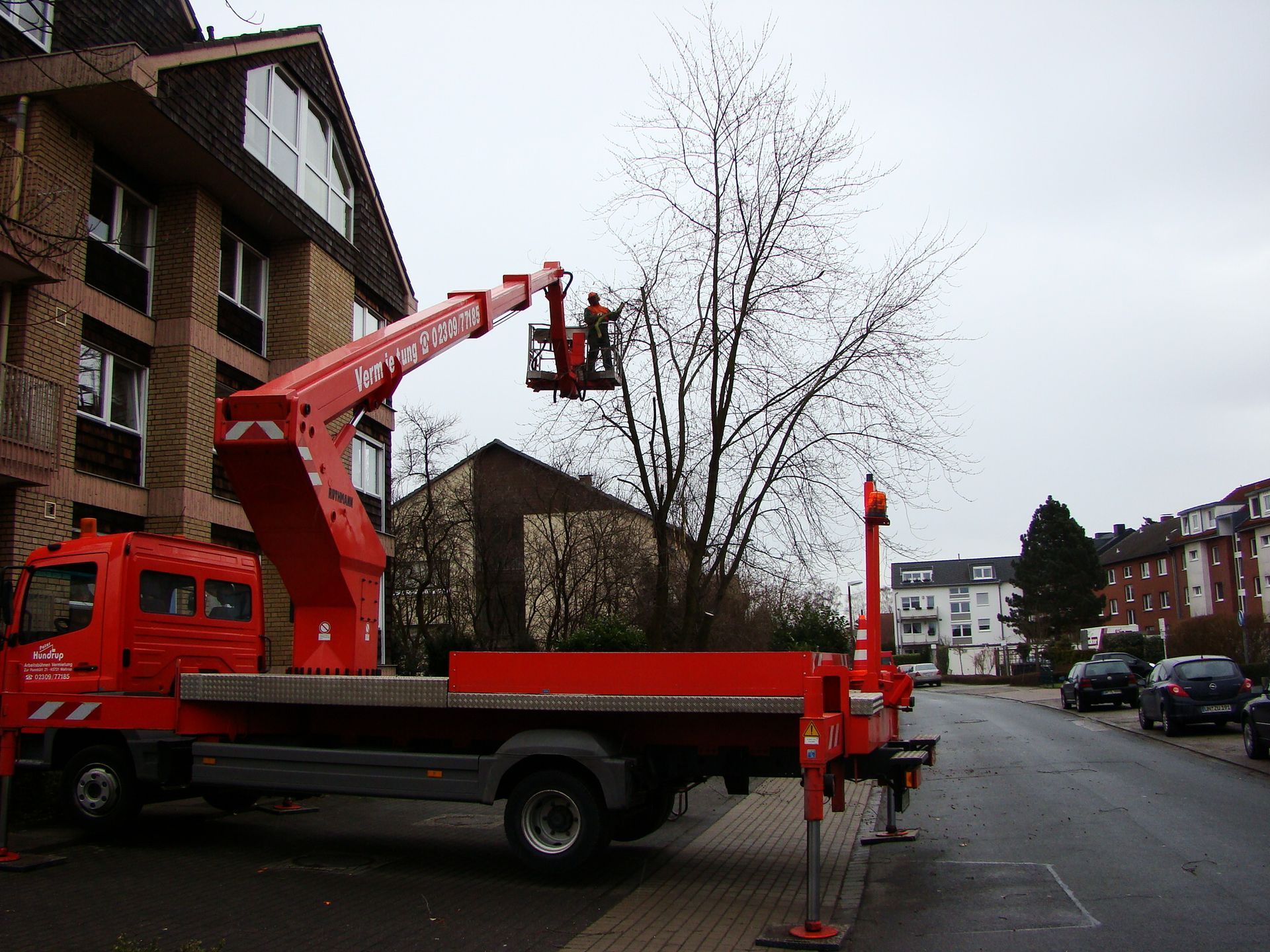 Ein roter LKW mit einem Kran auf der Rückseite ist vor einem Gebäude geparkt