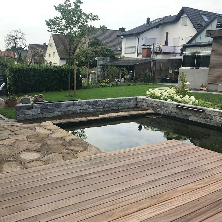 Eine Holzterrasse mit Blick auf einen Teich mit Häusern im Hintergrund