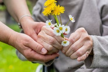 Ältere Person hält Blumen, geholfen von einer Pflegekraft