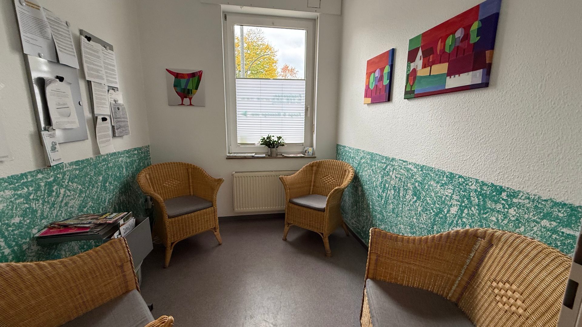 Freundlicher Warteraum mit Korbstühlen und farbigen Wandbildern.