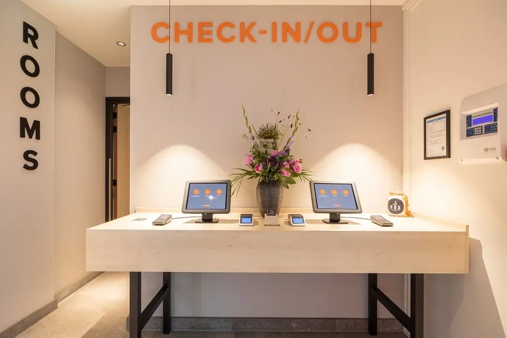 A check in / out desk in a hotel lobby with two computers and a vase of flowers.