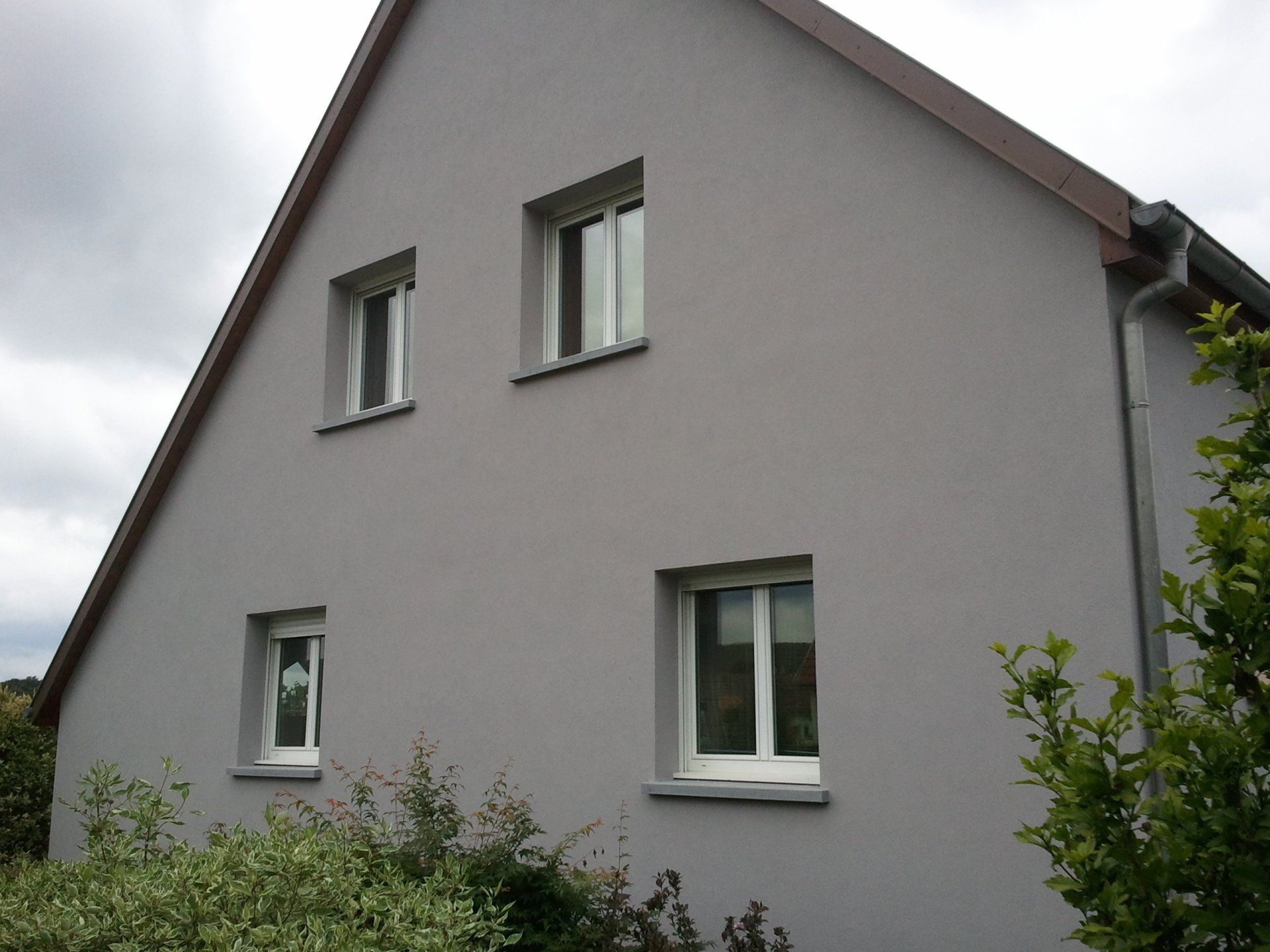 Maison grise avec fenêtres à cadre blanc.