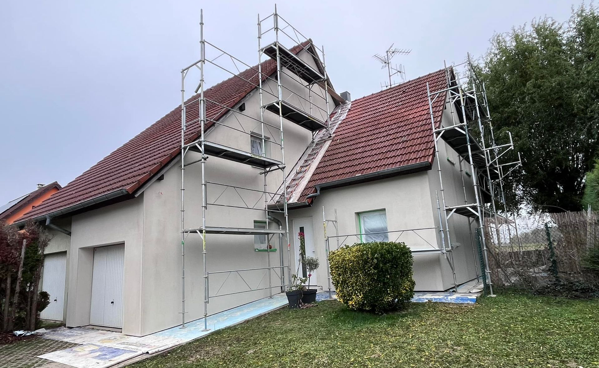 Extérieur de maison avec échafaudage, toit en tuiles rouges, murs clairs.