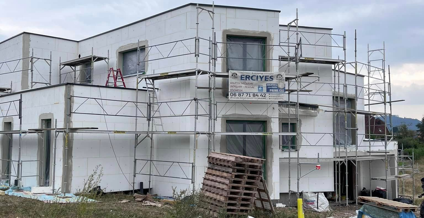 Bâtiment en construction, isolation extérieure blanche, échafaudage, fenêtres.
