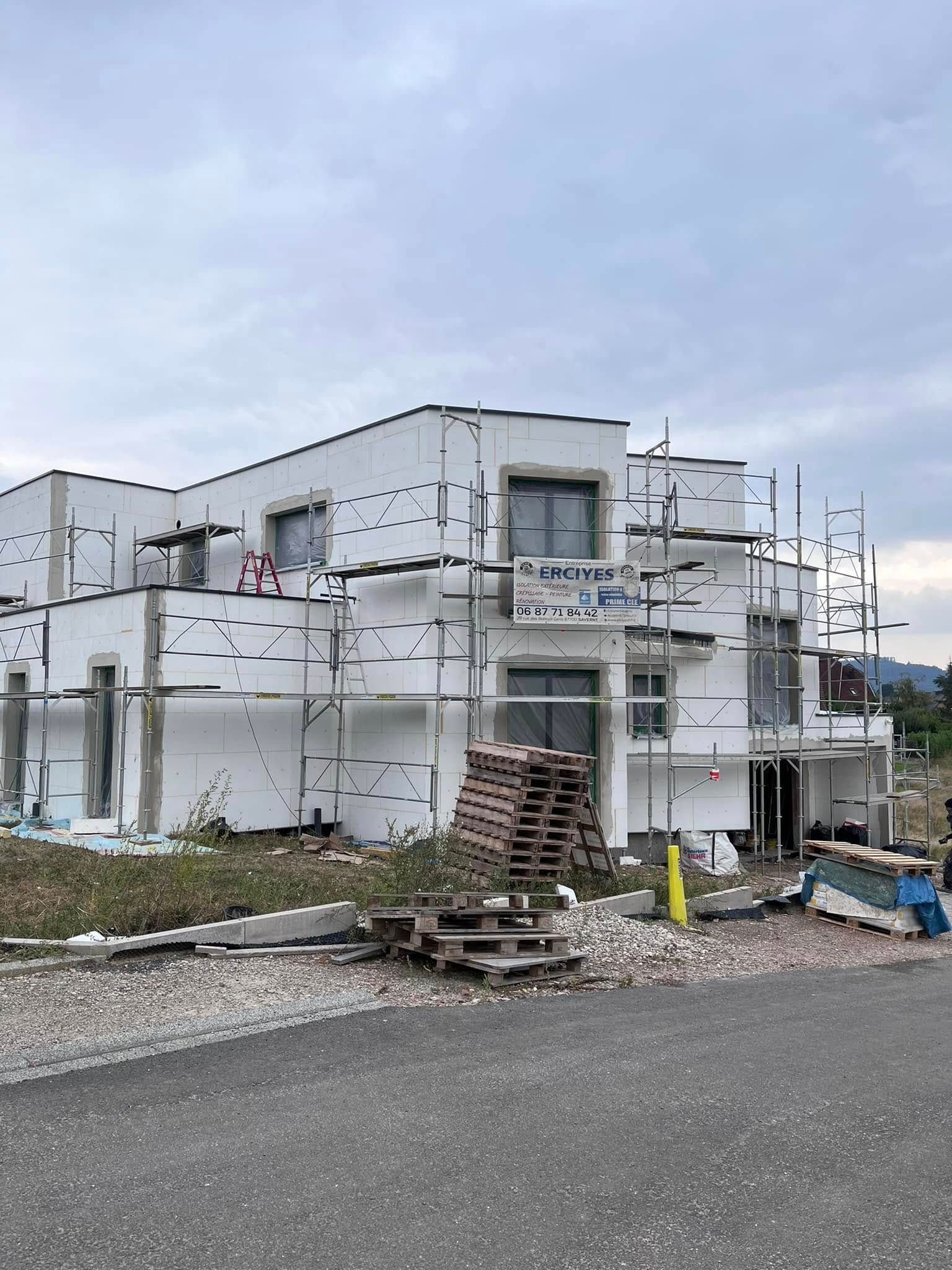 Bâtiment en construction avec échafaudage et panneaux isolants blancs.