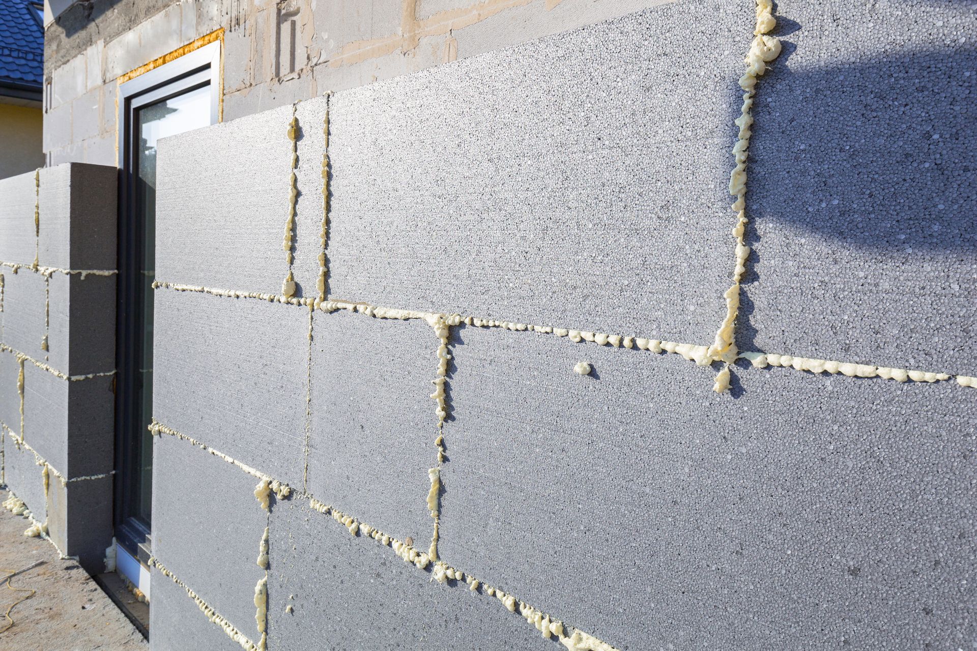 Construction de murs extérieurs avec panneaux isolants en mousse grise et mastic blanc.