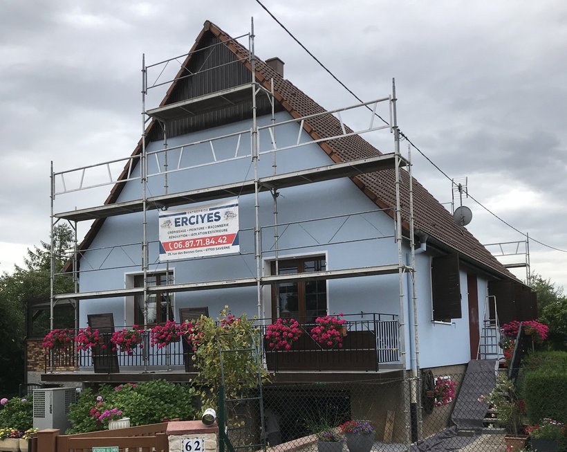 Maison en rénovation avec échafaudage, bardage bleu, bacs à fleurs.