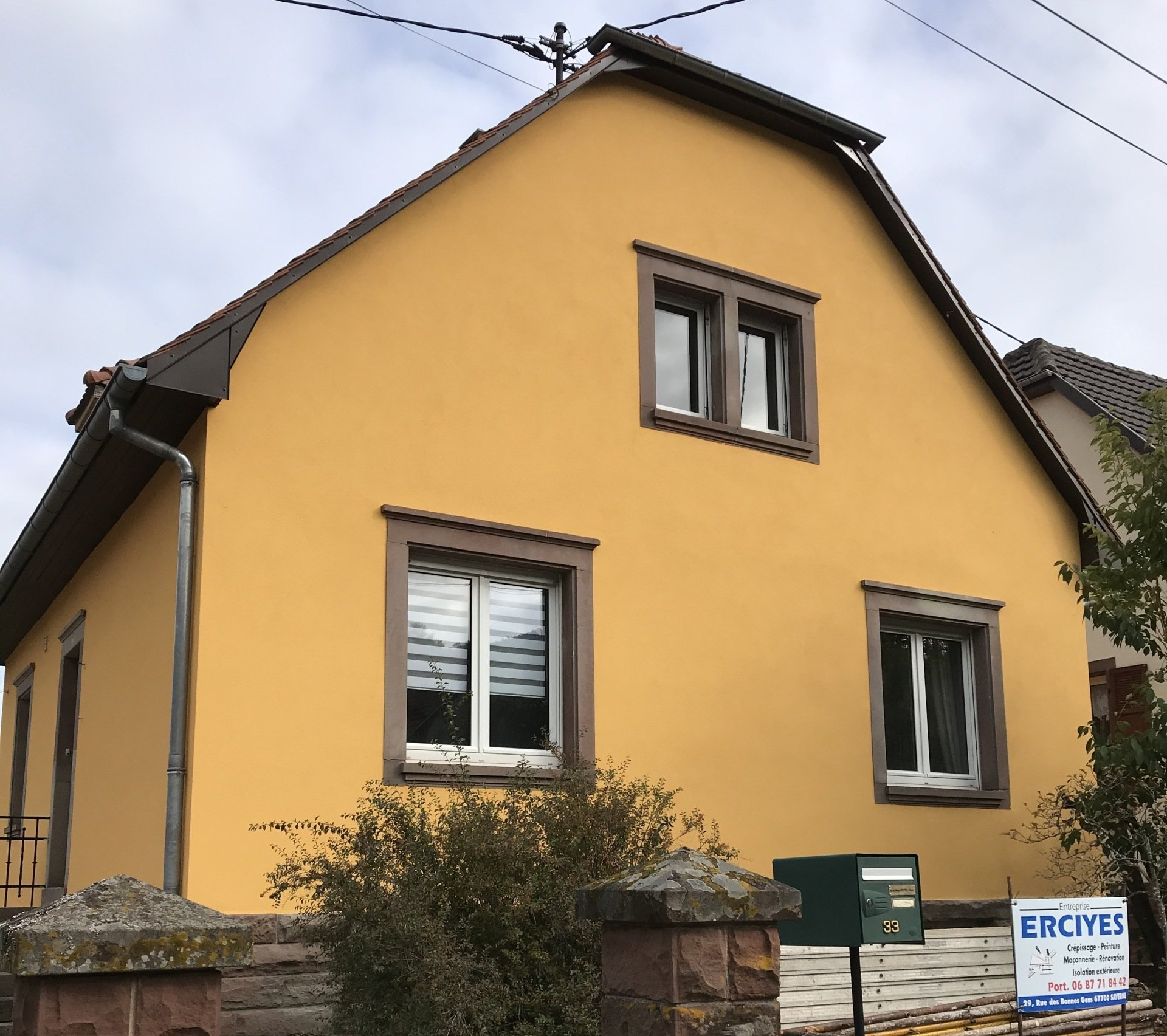 Maison jaune avec boiseries, fenêtres et toit marron.