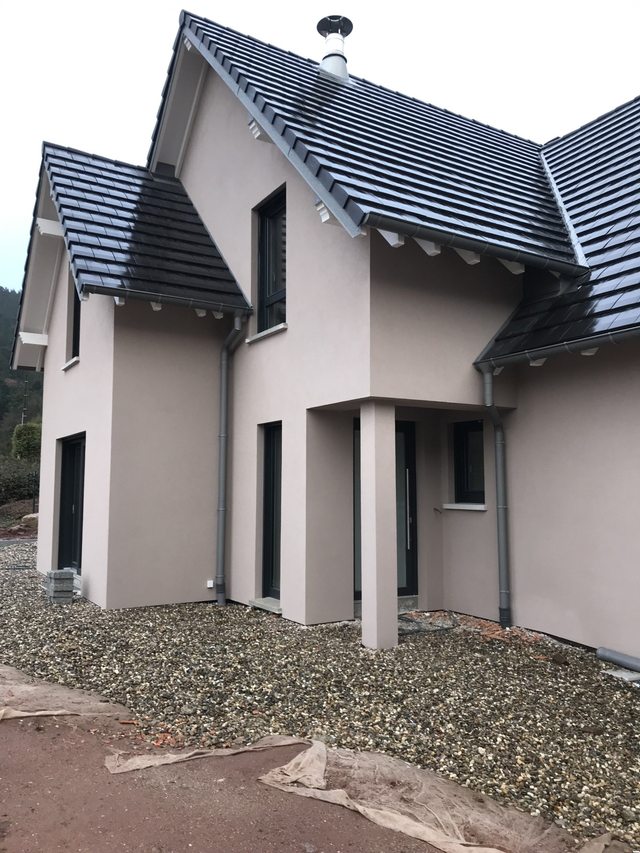 Maison en stuc beige avec des tuiles gris foncé et une cour en gravier.