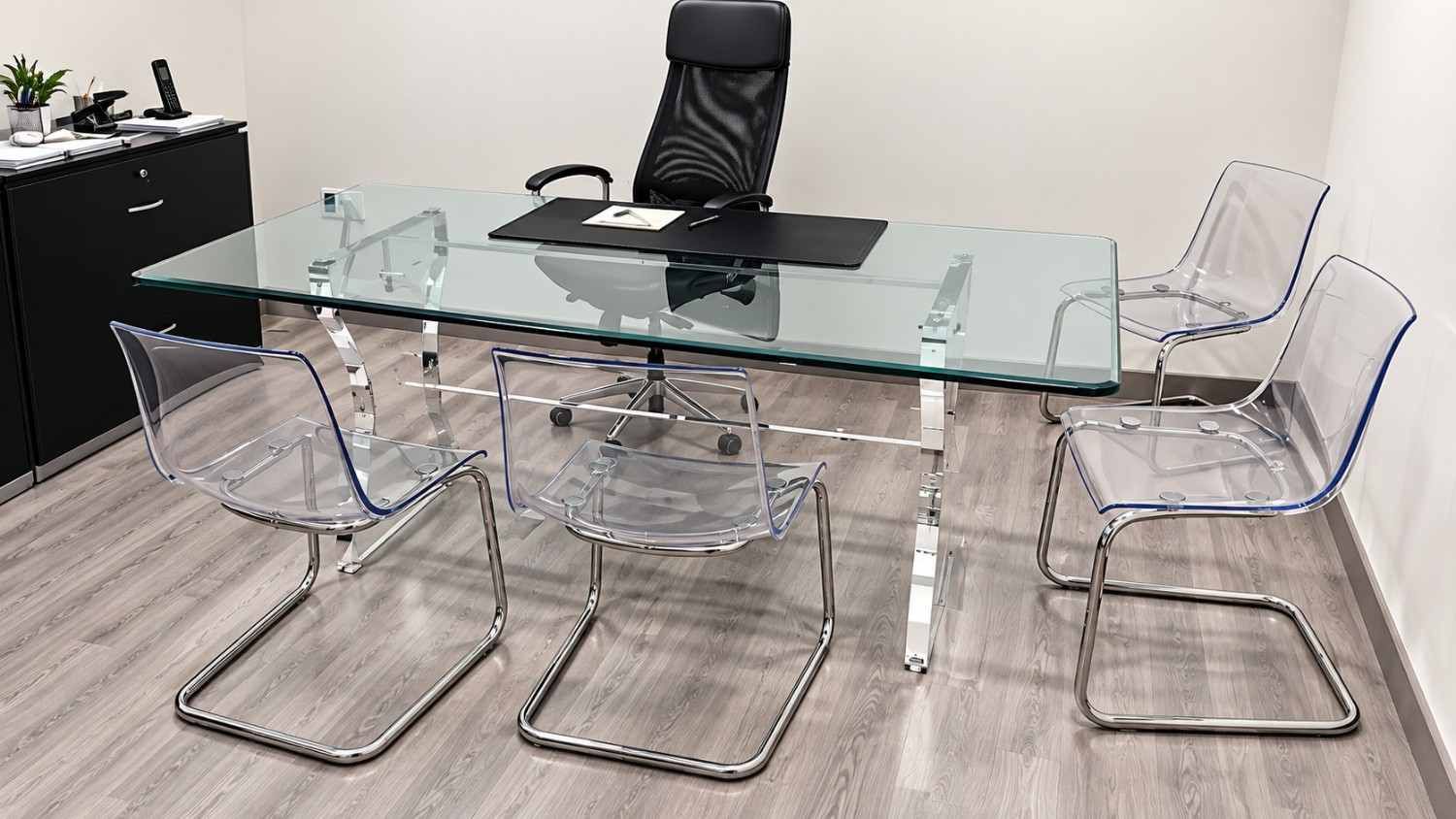 Mesa de conferencias de cristal con sillas de acrílico y una silla de oficina negra en una habitación moderna.