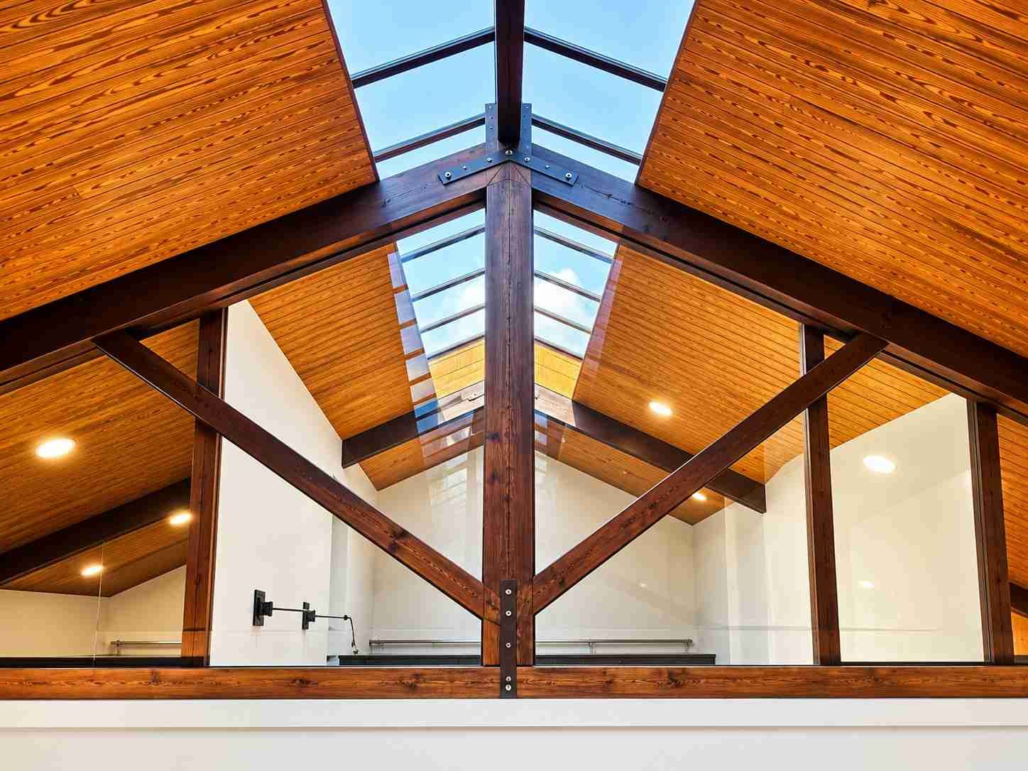 Interior del ático con vigas de madera, tragaluces y cálidos paneles de madera en el techo.