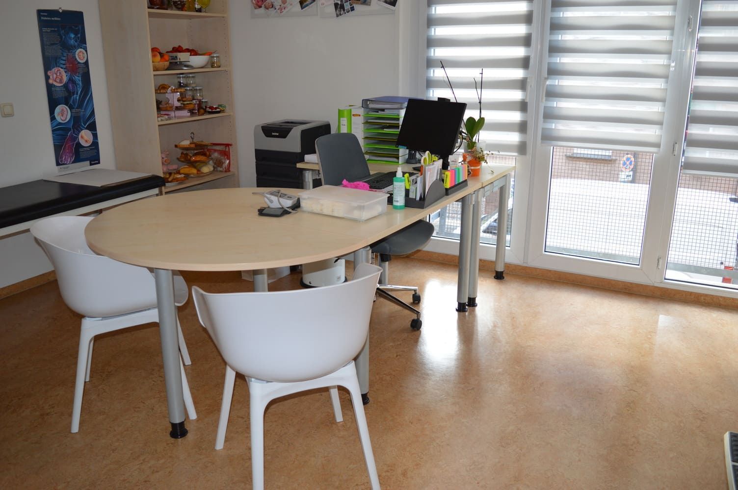 Büro mit hellbraunem Tisch, weißen Stühlen und großem Fenster. Man sieht Regale mit Snacks.