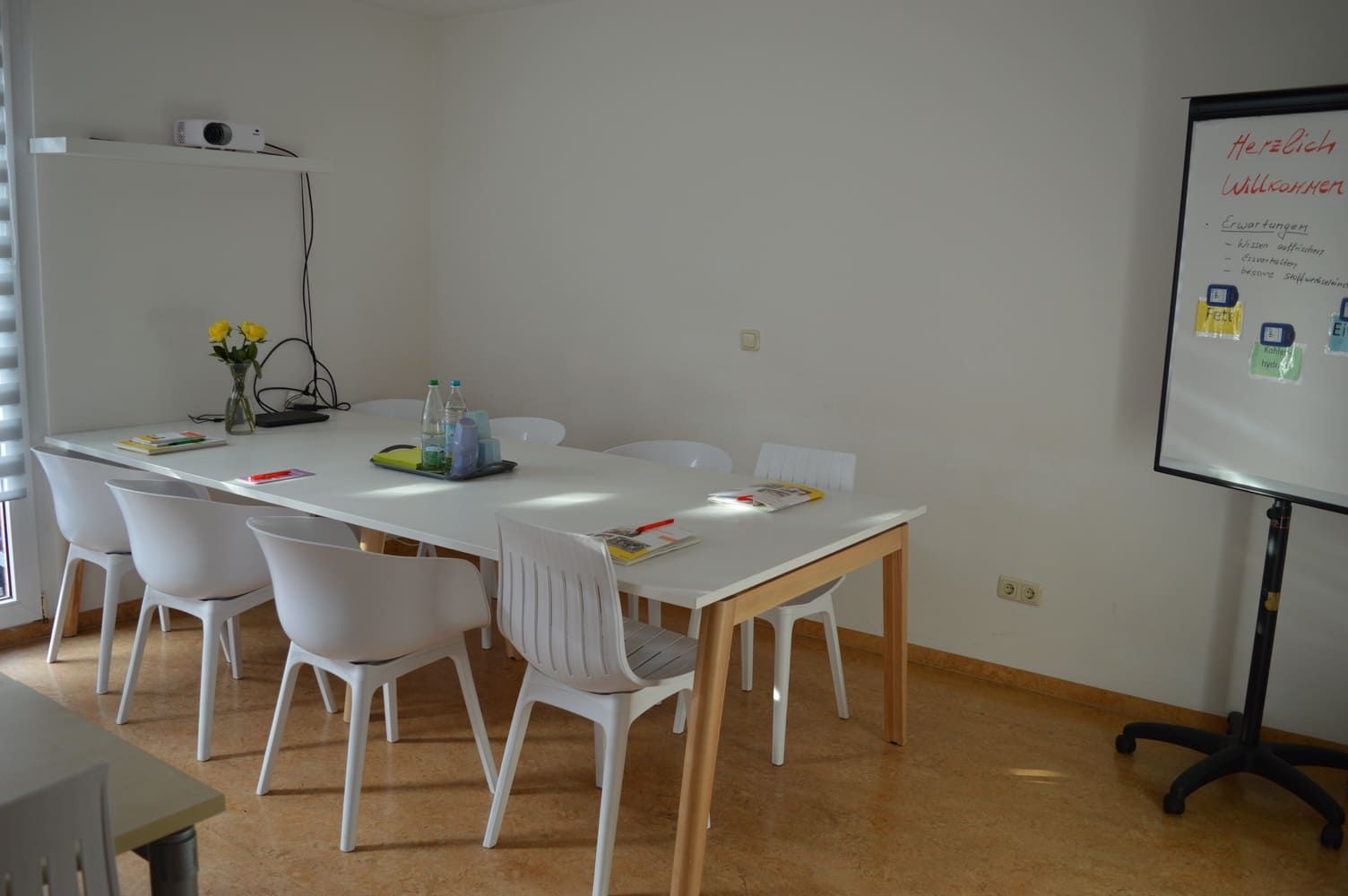 Besprechungsraum mit weißem Tisch, Stühlen, Whiteboard und Blumen.