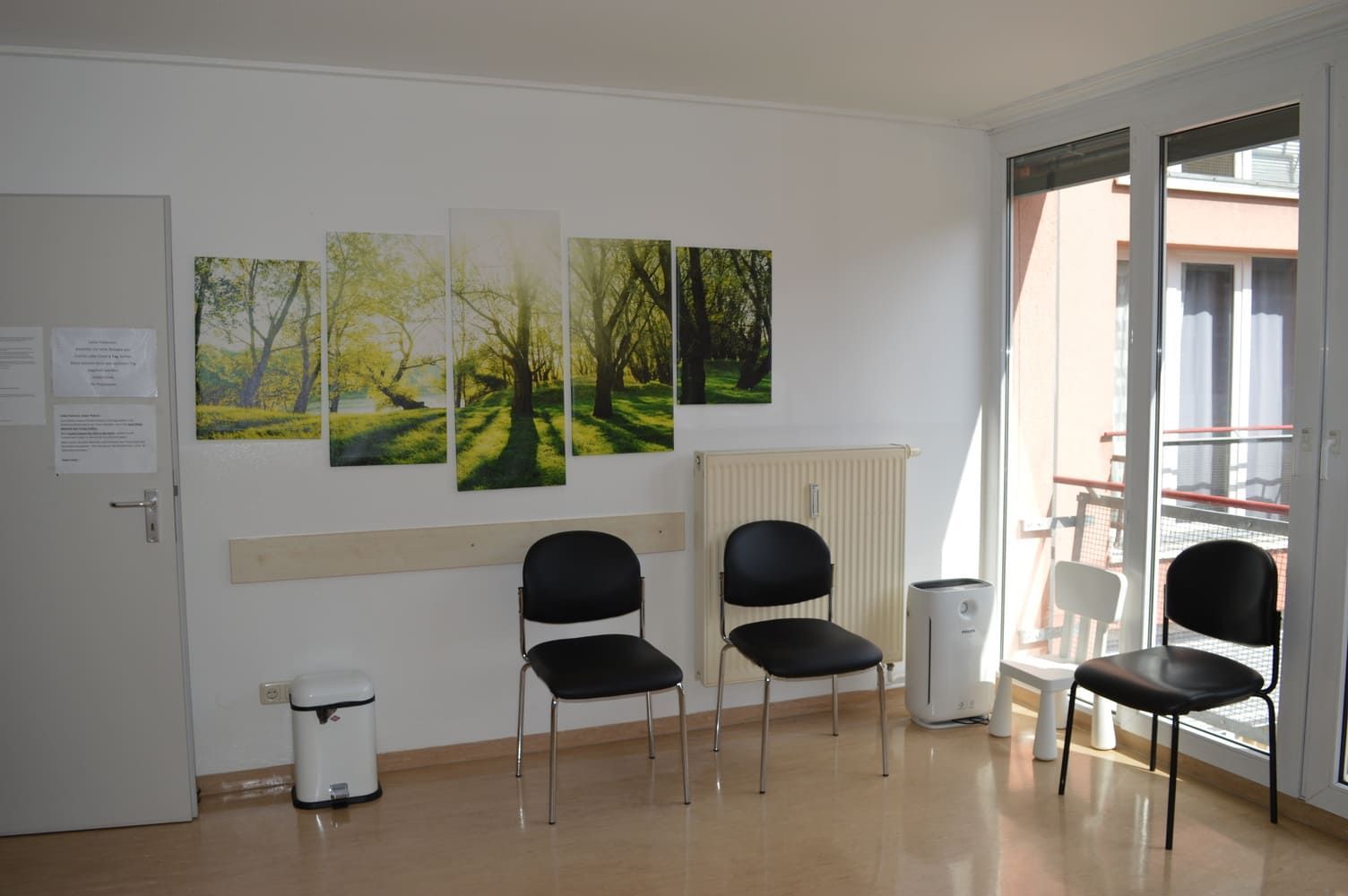 Wartezimmer mit schwarzen Stühlen, Wandkunst mit einem Wald und einem Fenster.