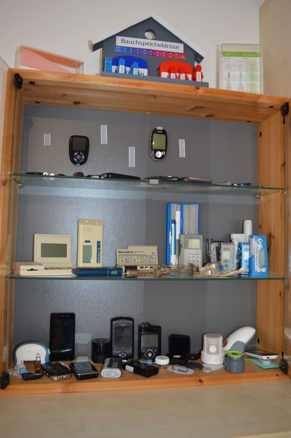 Holzvitrine gefüllt mit verschiedenen elektronischen Geräten und Gadgets, darunter Telefone, Messgeräte und andere Geräte.