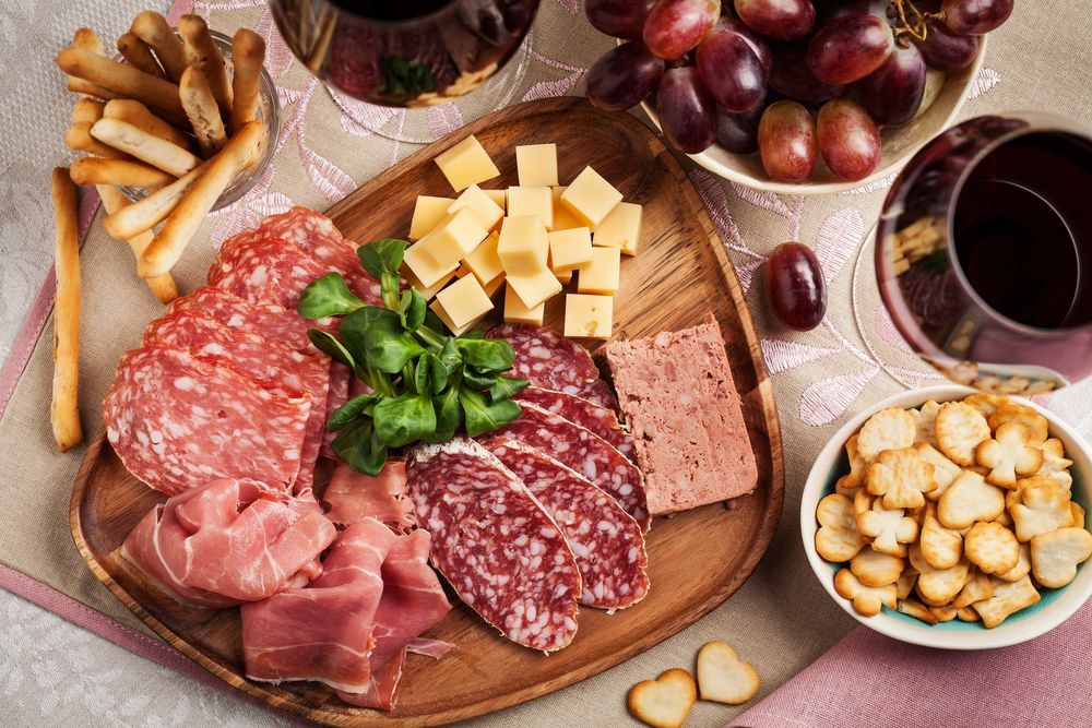 Una tabla de cortar de madera cubierta con carne, queso, galletas y uvas.