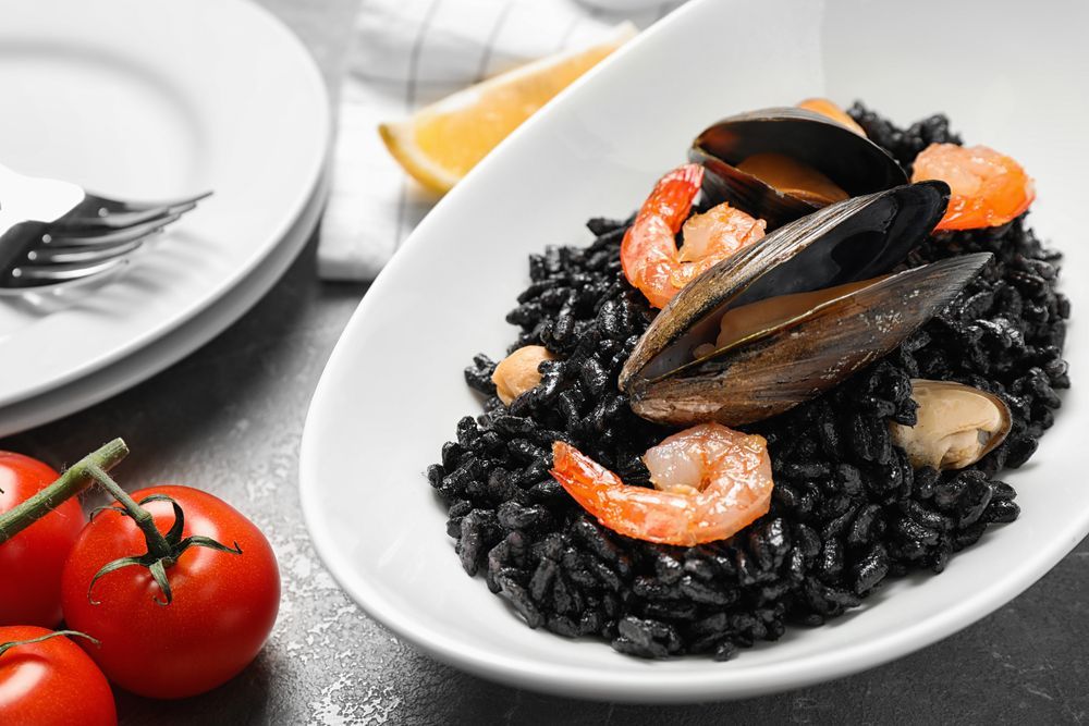 Un plato de arroz negro con camarones y mejillones en una mesa.