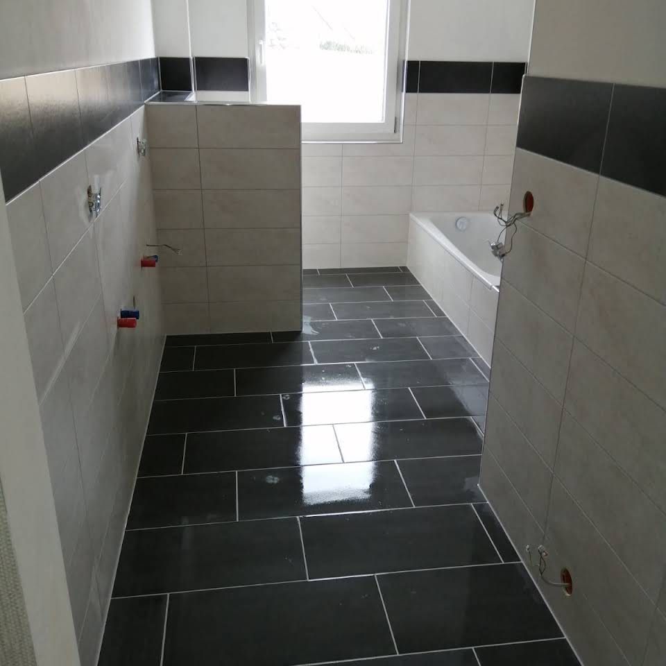 Ein teilweise renoviertes Badezimmer mit schwarzen Bodenfliesen, hellen Wandfliesen, einer schwarzen Bordüre und einer eingebauten weißen Badewanne.