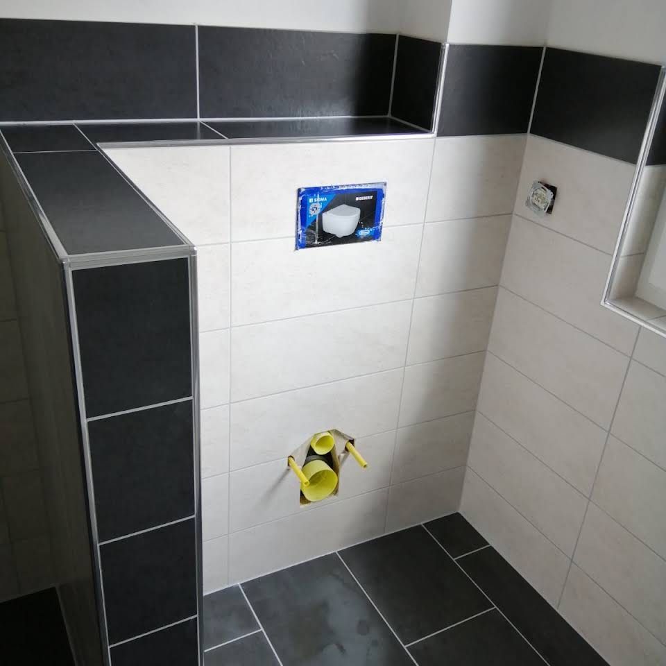 Eine im Bau befindliche Badezimmerwand mit weißen und schwarzen Fliesen, an der ein wandmontierter WC-Montagerahmen angebracht ist.