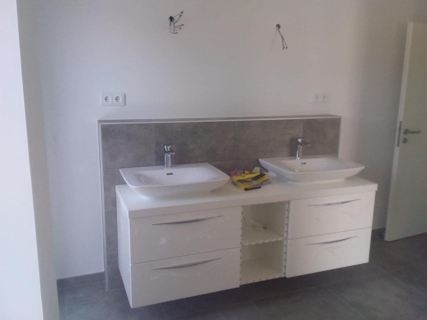 Ein moderner, wandmontierter Doppelwaschtisch mit weißen Schränken, zwei Aufsatzwaschbecken und einem grauen Fliesenspiegel.