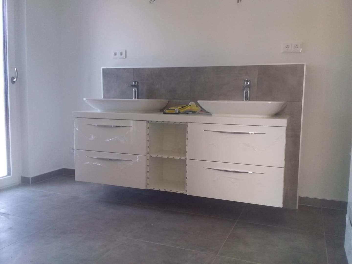 Moderner, wandmontierter Doppelwaschtisch mit weißen Schränken und zwei Aufsatzwaschbecken vor einem grauen Fliesenspiegel.