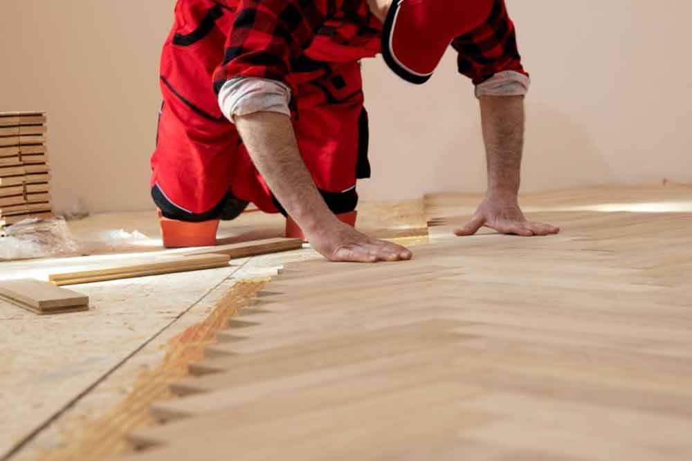 Person, die Hartholzböden verlegt. Roter Overall, Kappe, konzentriert bei der Arbeit.