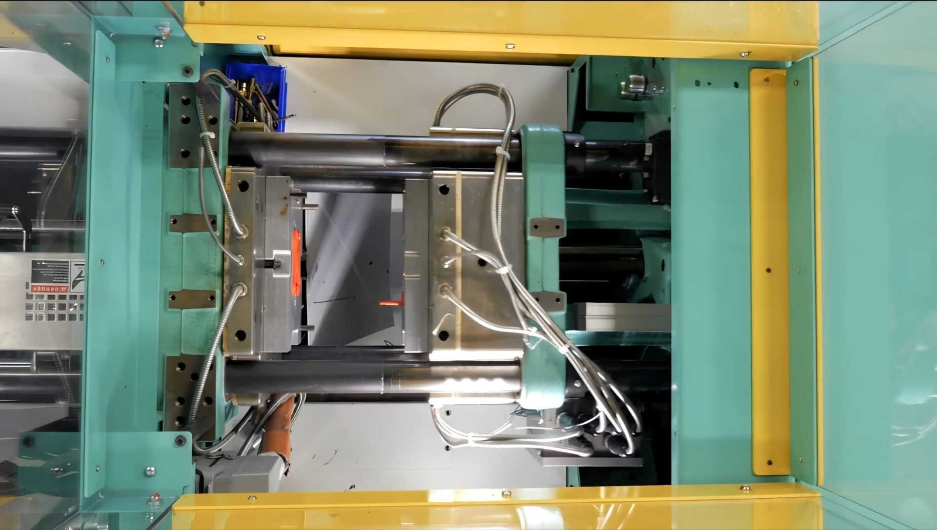 Interior de una máquina industrial con estructura verde y amarilla, componentes metálicos y mangueras
