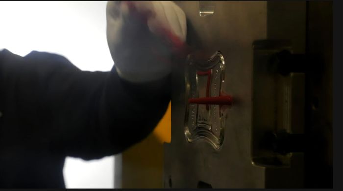 La mano de una persona girando una palanca roja en un pestillo de metal en una habitación con poca luz.