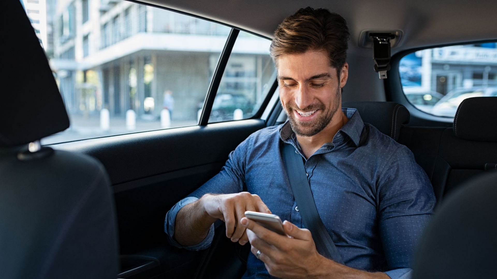 Un homme dans une voiture, souriant et regardant son téléphone.