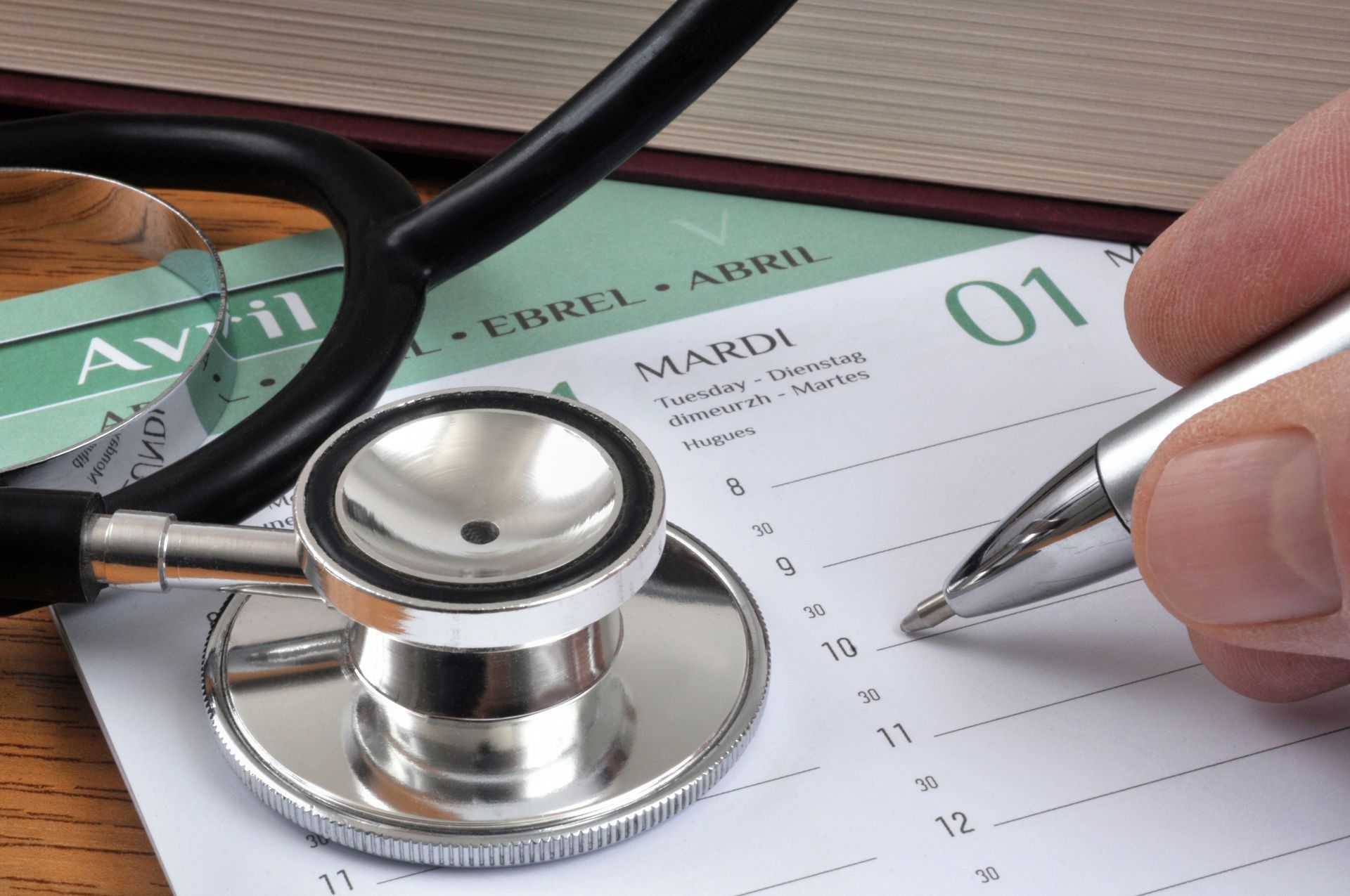 Un stéthoscope sur un calendrier, avec une main tenant un stylo.