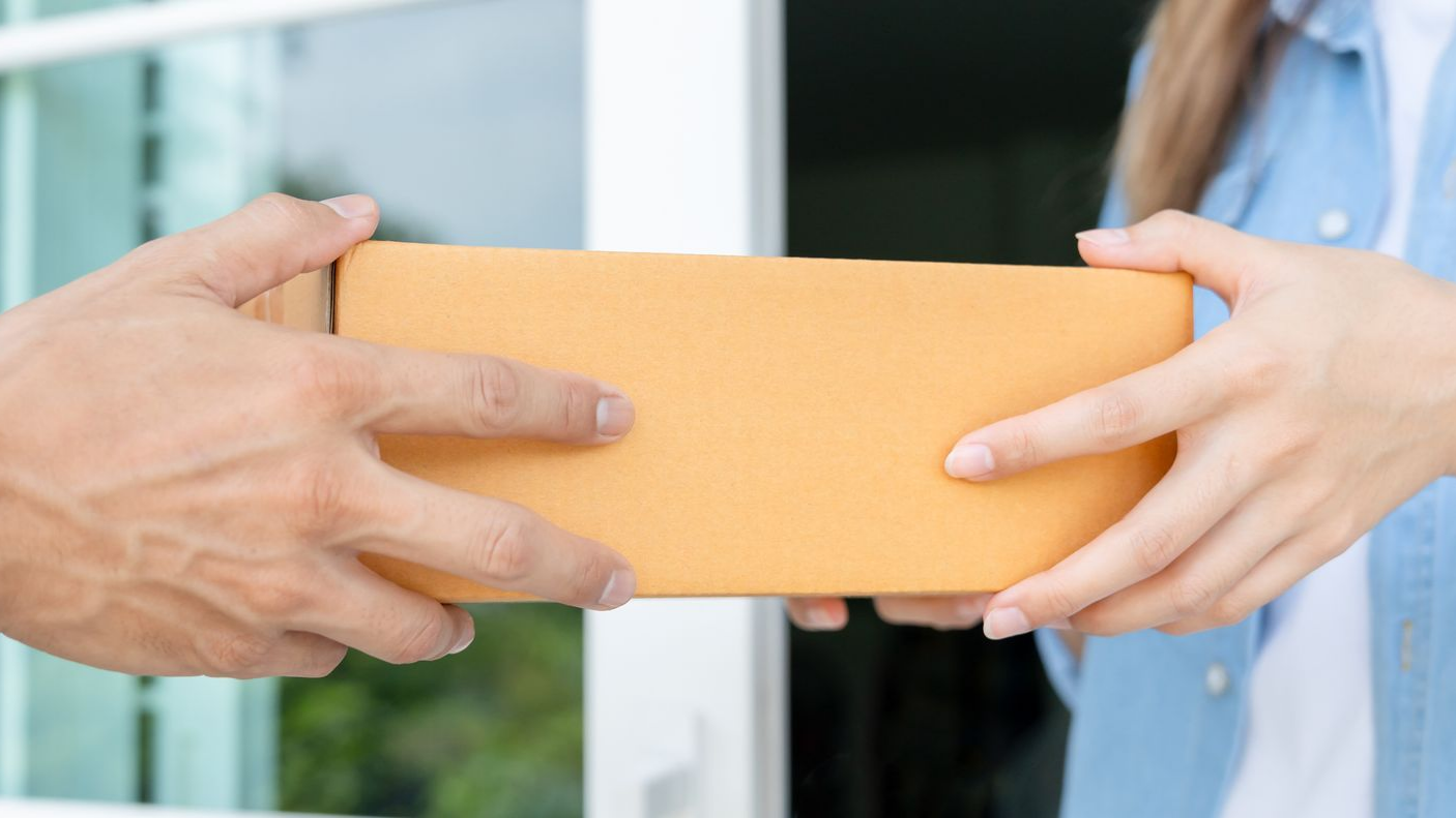 Des mains échangent une boîte en carton brun devant une porte.