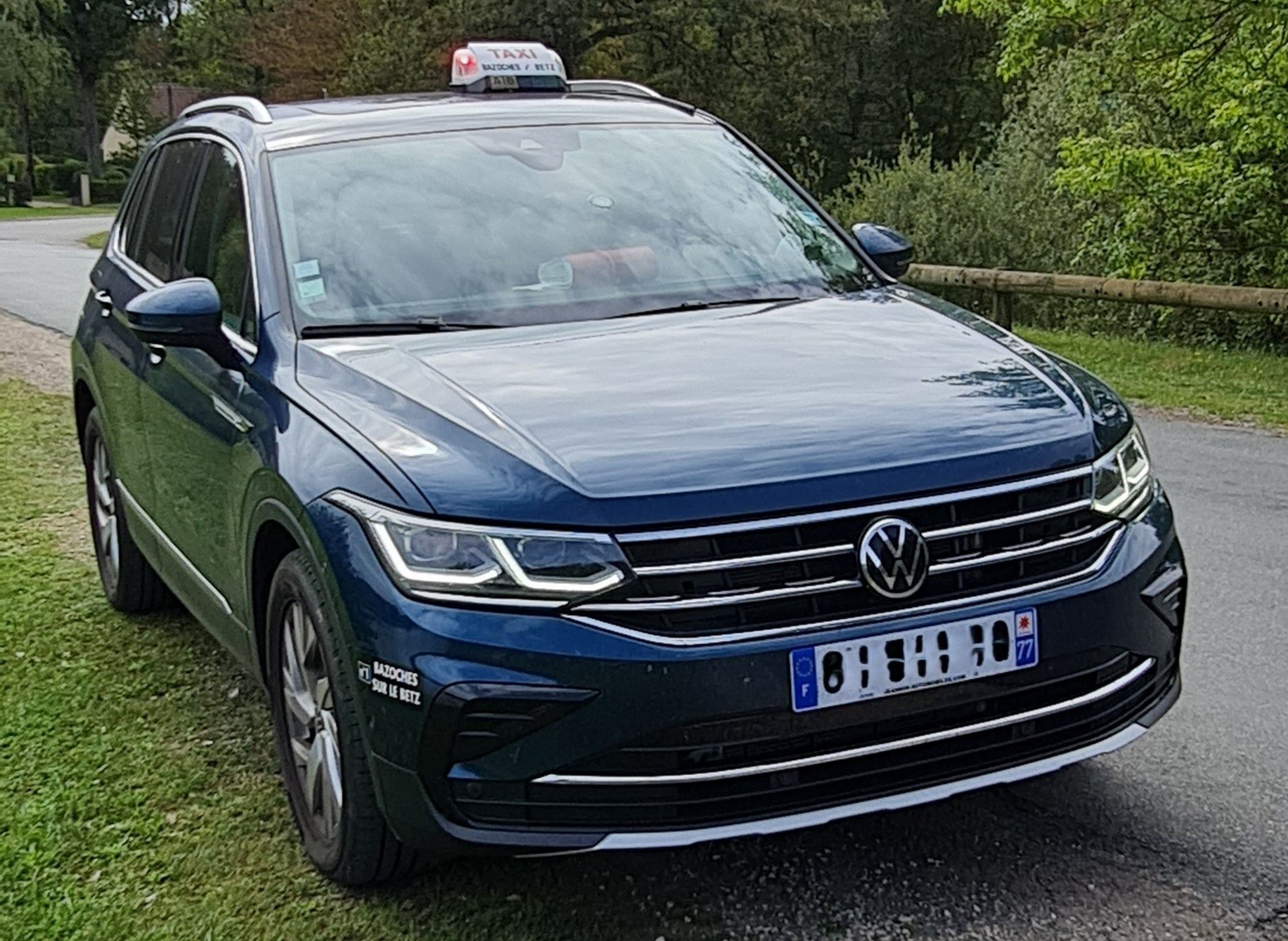 Un taxi Volkswagen Tiguan bleu est stationné en bord de route avec un panneau taxi sur le toit.