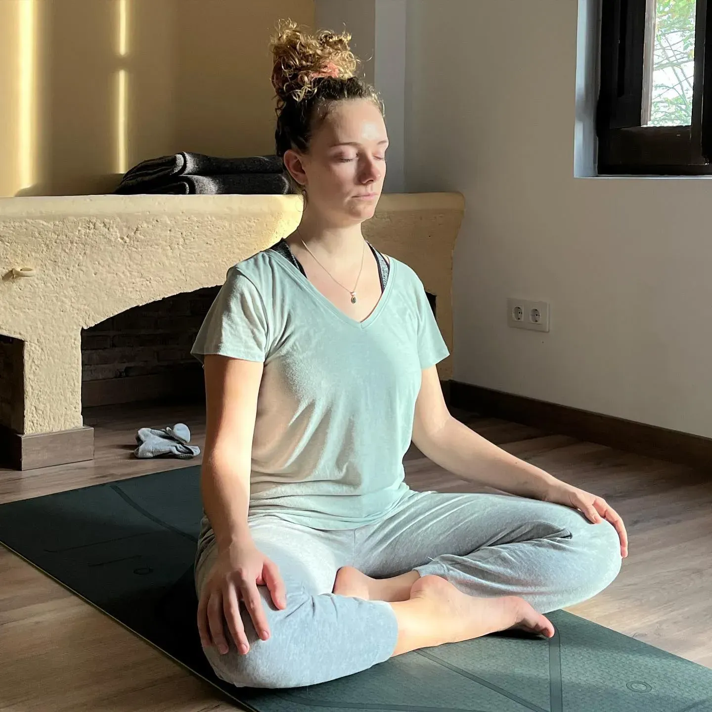 Una mujer está sentada en una esterilla de yoga con los ojos cerrados.