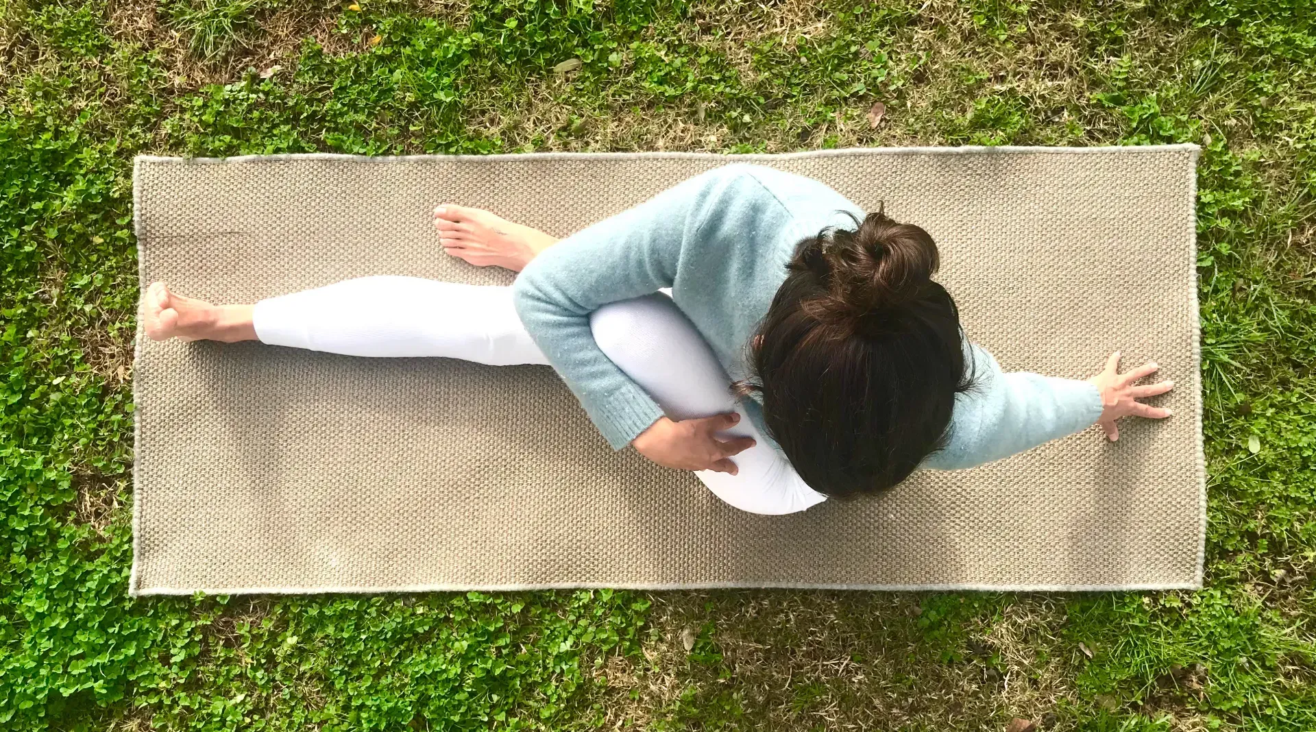Una mujer está tumbada sobre una colchoneta de yoga en el césped.