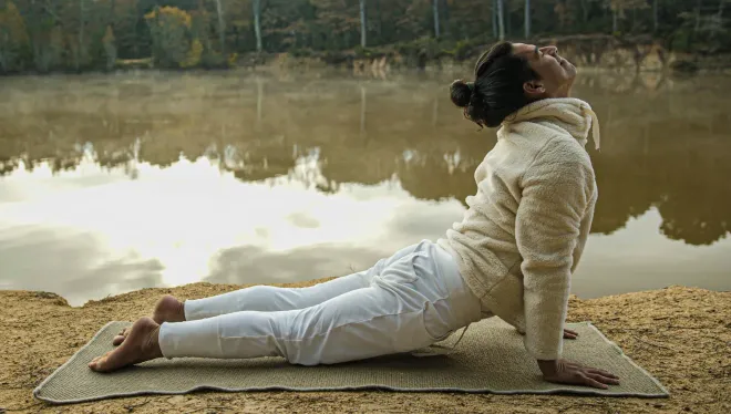 Una mujer está haciendo yoga en una colchoneta cerca de un lago.