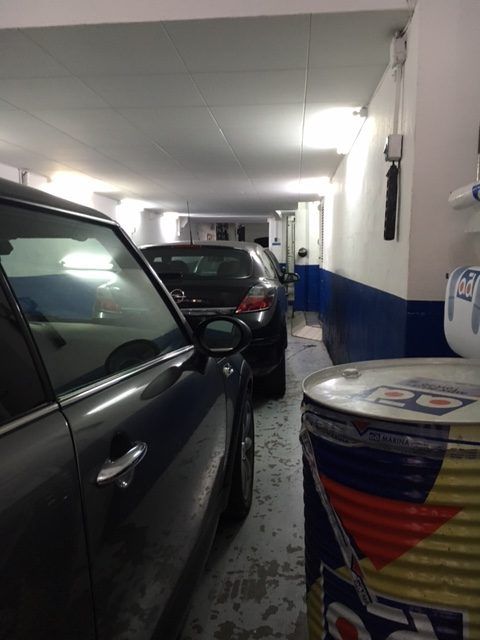 Coches aparcados en un estrecho garaje, con un bidón de aceite en primer plano.