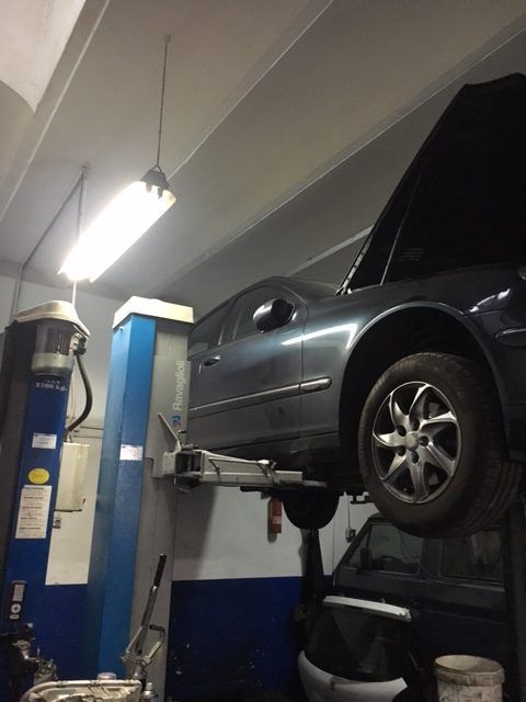 Coche en un elevador en un garaje con el capó abierto, iluminado por luces fluorescentes en el techo.