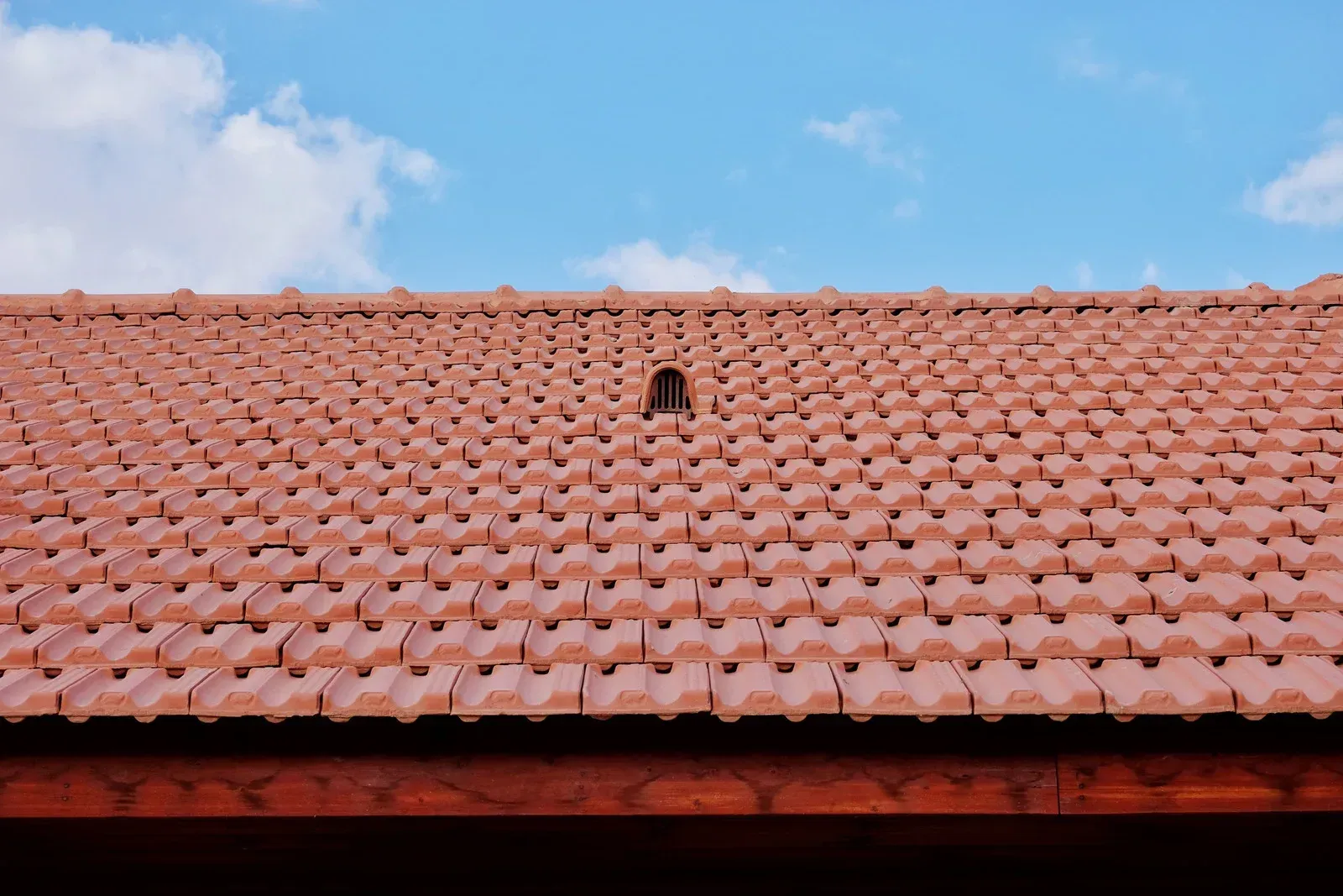 Terracotta tile roof under a blue sky with a small vent near the ridge