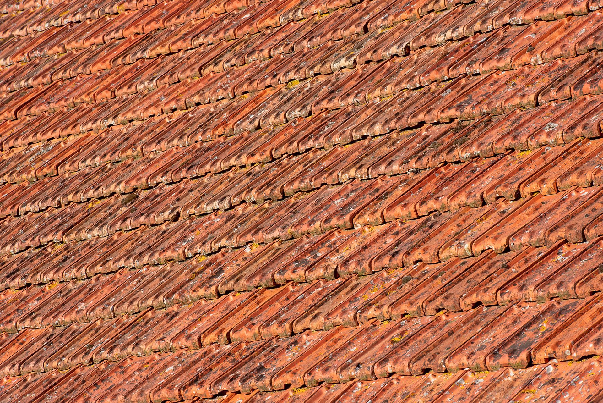 Close-up of weathered orange-brown tiled roof with diagonal rows and shadows