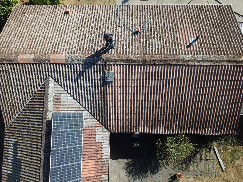 Aerial view of a tiled roof with two workers and solar panels on a lower roof section.