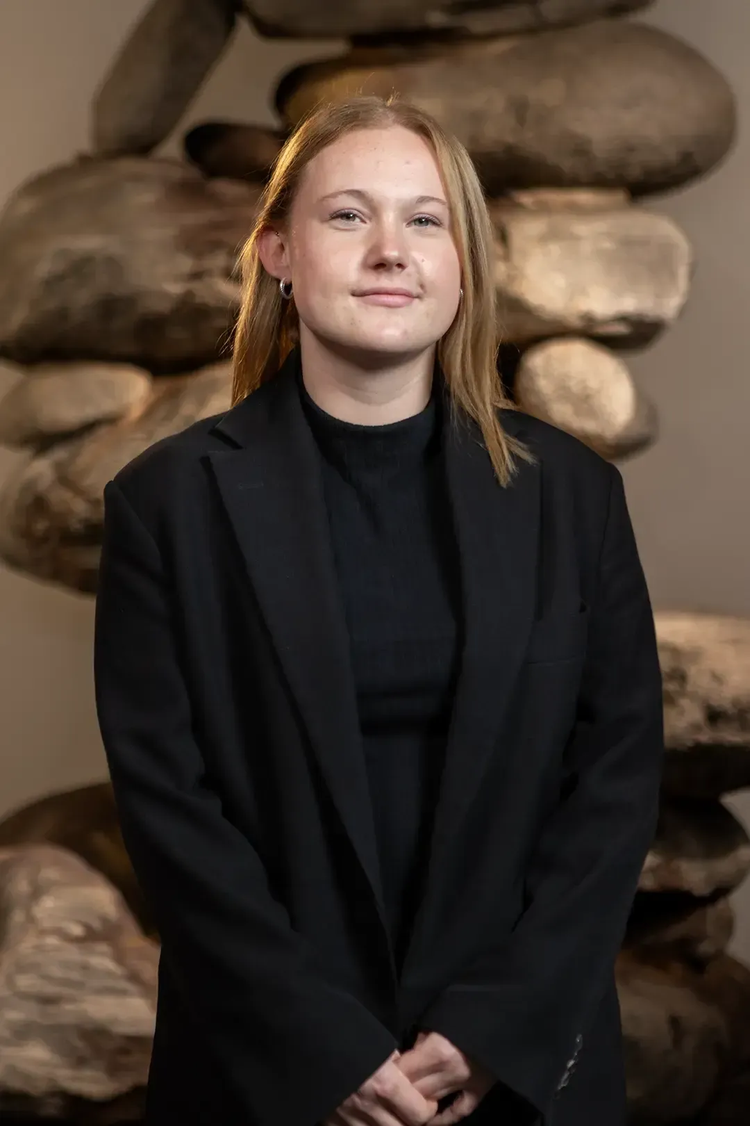 Eine junge Frau mit einem schwarzen Rollkragenpullover und Ohrringen blickt in die Kamera.