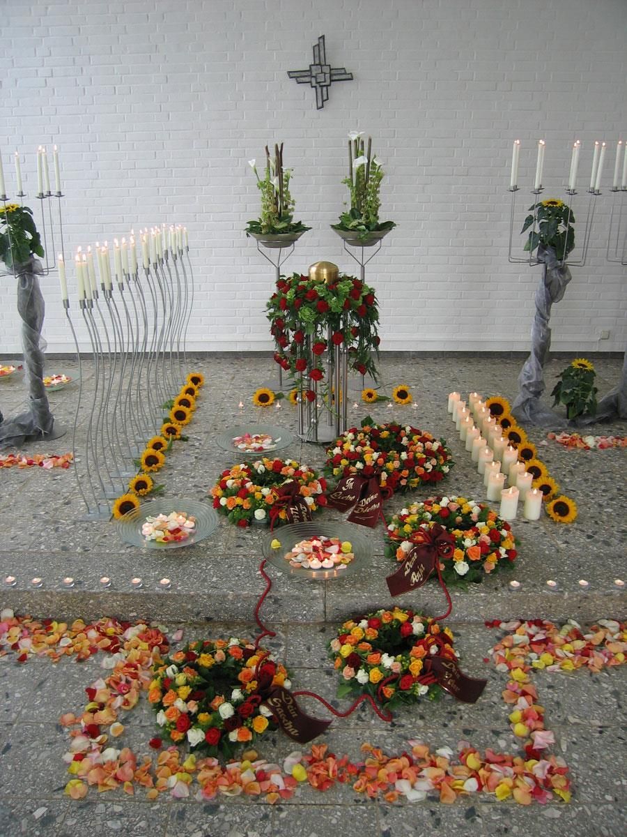 Eine Präsentation von Blumen und Kerzen mit einem Kreuz an der Wand