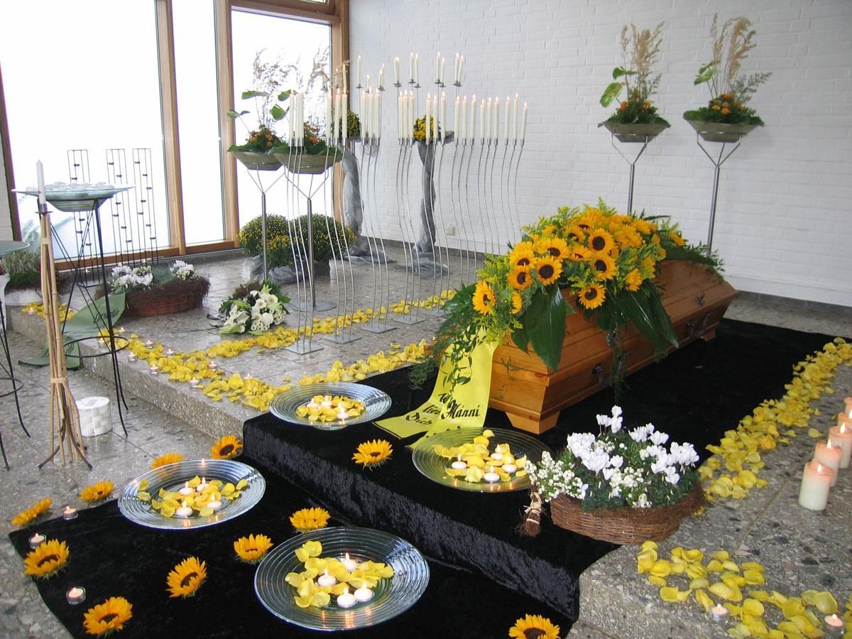 Ein Sarg ist mit gelben Blumen und Kerzen geschmückt
