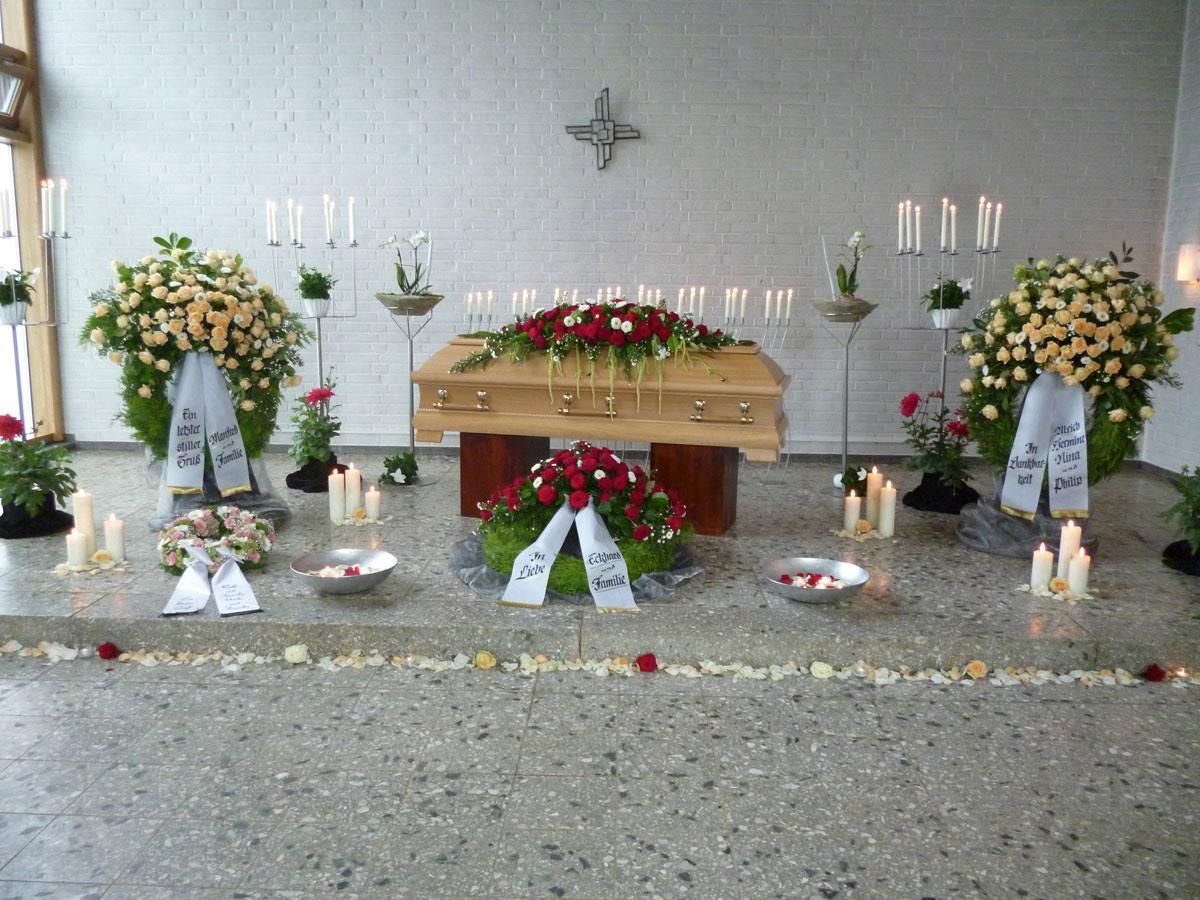 Ein Sarg ist in einem Raum von Blumen und Kerzen umgeben