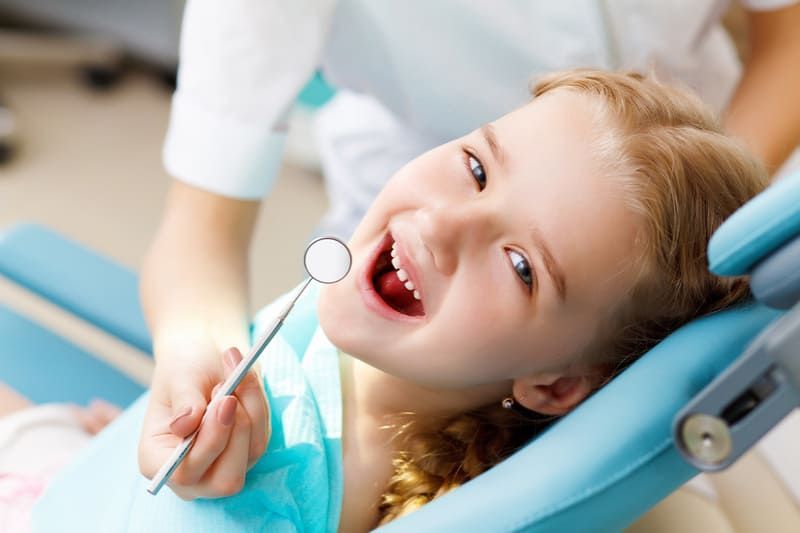 Ein kleines Mädchen sitzt in einem Zahnarztstuhl und lächelt | Zahnärzte am Westkreuz