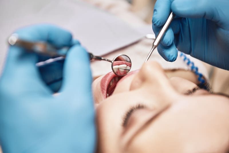 Ein Zahnarzt untersucht die Zähne einer Frau mit einem Spiegel | Zahnärzte am Westkreuz