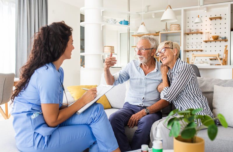 Eine Krankenschwester spricht mit einem älteren Paar auf einer Couch | Zahnärzte am Westkreuz