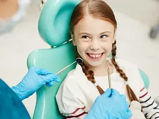 Una niña está sentada en una silla dental mientras un dentista le examina los dientes.