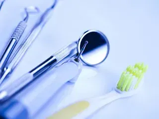 Un cepillo de dientes, un espejo, pinzas e instrumentos dentales sobre una mesa.